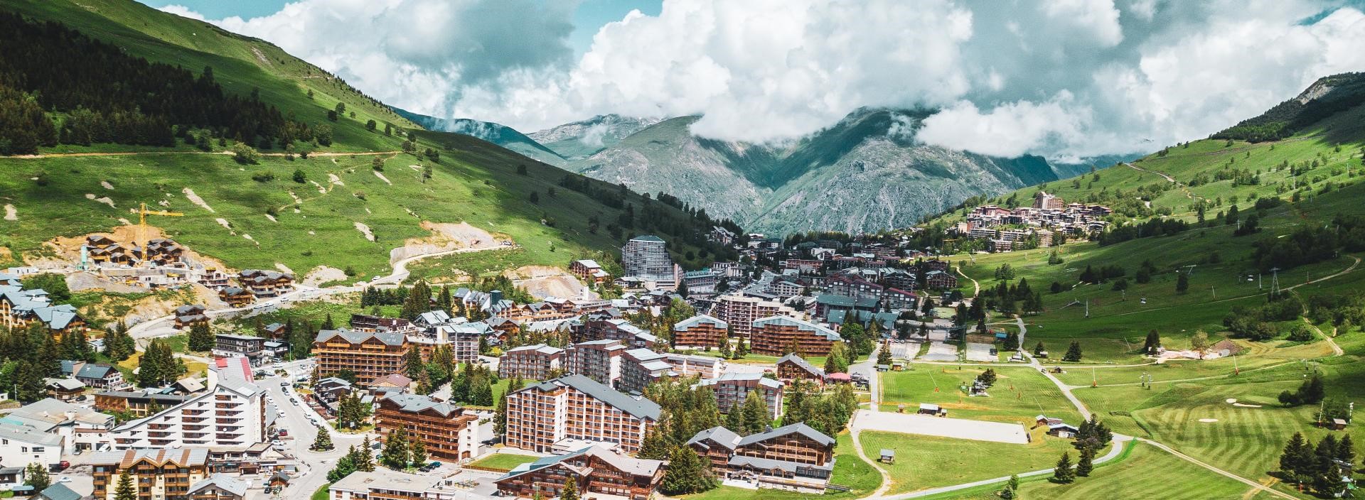 Commune des 2 alpes avec des batime,ts au premier plan et la Muzelle en arrière plan dans les nuages